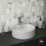 Round white vessel sink with a modern silver faucet on a dark countertop, marble hex tile backsplash, with diffuser and soap dispensers nearby.